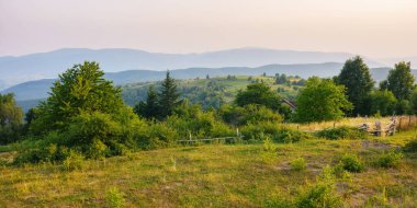 Yazın kırsal dağ manzarası. Dalgalı tepelerde ağaçlar ve çayırlarla vadiyi göz kamaştıran gün batımı manzarası