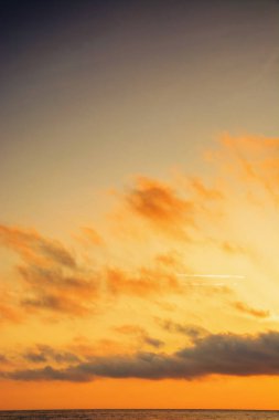 Denizde altın gün doğumu. Yumuşak bulutlar ufuktaki güneşi kaplar. Yaz tatilinde iyi hava tahmini