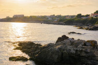 Gündoğumunda taşlı Karadeniz manzarası. Yaz tatili sezonu. Hava bulutlu. Güneş ışığı su yüzeyine yansıyor.