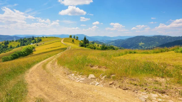 丘の下の田舎道と遠くの谷に転がり込む草の牧草地 夏の晴れた日にウクライナのカルパチア人の山岳地帯の風景 — ストック写真