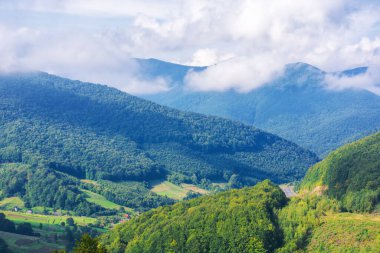 Sonbaharda dağlık bir Karpatya kırsalında. Orman tepeleri uzak kırsal vadiye doğru iniyor. Gökyüzünde bulutlar olan güneşli bir günde güzel bir manzara.
