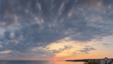Denizde dramatik bir şafak. Gökyüzünde gri bulutlar ve ufukta kırmızı güneş. Yaz tatili yağmurlu hava tahmini