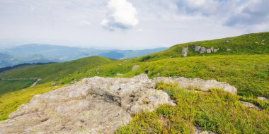 Yamaçtaki çimlerin arasında taşlarla dolu çayır. Güneşli bir öğleden sonra. Yazın dağlık kırsal alan. Sabahın ilk ışıklarıyla uzak kırsal vadiye bakın. Ukraynalı Karpatların güzelliği
