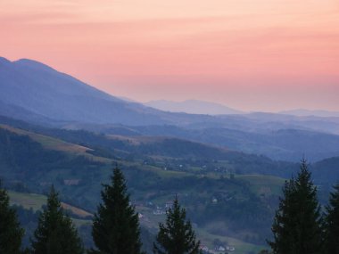 Karpat dağlarında gün batımı. Puslu bir atmosferde ormanlık yamaçlar arasında kayan tepeleri olan uzak kırsal vadi. pembe gökyüzü