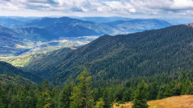 Sonbaharda dağlık bir Karpatya kırsalında. Orman tepeleri uzak kırsal vadiye doğru iniyor. Bulutlu bir günde gökyüzünde bulutlarla güzel bir manzara.