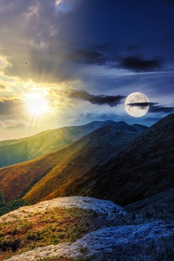 Tepenin tepesindeki çimlerin arasında taşlarla kaplı dağ manzarası bulutlu yaz gökyüzünün altında alacakaranlıkta güneş ve ay ile birlikte. Gündüz ve gece zaman kavramını değiştirir. Sabah ışığında gizemli bir manzara.