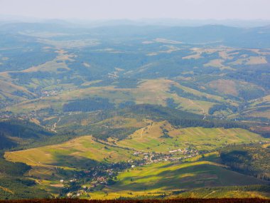 Yazın sonlarında dağlık bir manzara. Tepenin tepesinden vadideki köye bak. Güneşli bir öğleden sonra güzel bir kırsal arka plan