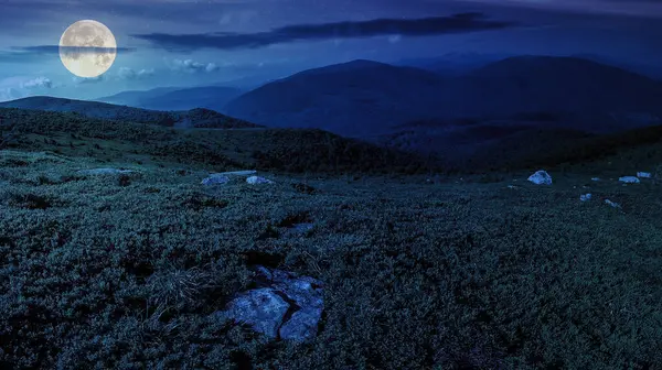 mountain panorama landscape at night. stones in grass on top of the hillside of mountain range. wonderful countryside scenery in full moon light