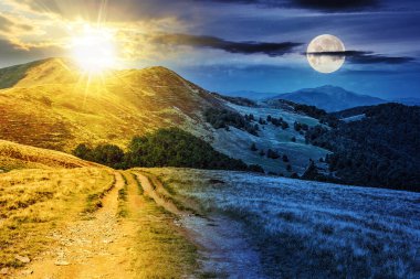 Alacakaranlıkta güneş ve ay ile dağ sırasındaki geniş çayır boyunca yol. Gündüz ve gece zaman kavramını değiştirir. Gizemli kırsal manzara Sabah ışığında