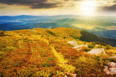 Gün batımında dağlık bir manzara. Tepenin kenarındaki çimenlikte taşlarla dolu çayır. Uzaktaki vadiye bak. Akşam ışığında güzel doğa manzarası