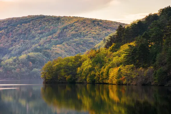 Gün batımında gölü olan dağlık sonbahar manzarası. Durgun suya yansıyan sonbahar renklerindeki manzara