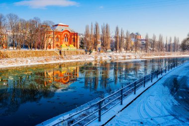 Uzhgorod kışın şehir manzarası. Karla kaplı toprak seti olan şehir manzarası. Nehre yansıyan eski bir sinagogun kırmızı binası. Güneşli bir günde soğuk hava