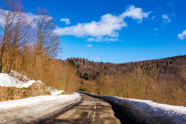 Eski yol karla kaplı tepelerden geçer. Güneşli bir günde, bulutlu mavi gökyüzünün altında, dağlık kış manzarası.