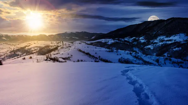 mountainous landscape at winter solstice in morning light. scenery with snow covered hills and leafless forest in the distance beneath a sky with sun and moon. day and night time change concept