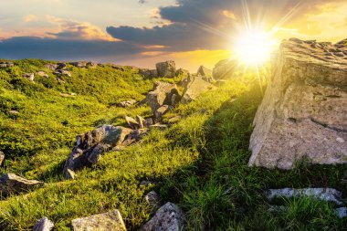 Gün batımında dağ manzarası. Yamacın tepesindeki çimlerin arasında kocaman taşlar olan çayır. Güzel kırsal manzara Akşam ışığında