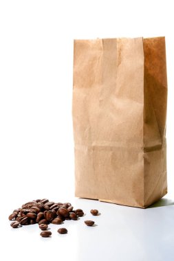 Kavrulmuş kahve çekirdekleri beyaz arka plandaki el işi kağıdından yapılmış kahverengi bir kullan-at paketin önüne döküldü. Çevre dostu markalaşma için geri dönüşümlü ve sürdürülebilir modelleme kavramı