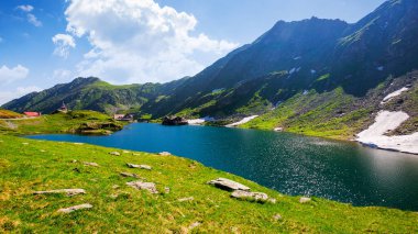 İbne dağlarının alp manzarası. Yazın Romanya 'nın Balea Gölü. Mavi gökyüzünde bulutlu güneşli bir hava. Kayalık yamaçta kar ve çimen lekeleri