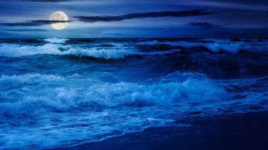 Gece dramatik deniz manzarası. Dalgalar dolunay ışığında sahile çarpıyor.