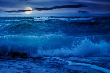 Gece dramatik deniz manzarası. Dalgalar dolunay ışığında sahile çarpıyor.