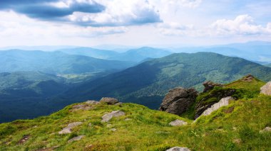 Yazın Karpatlar 'ın dağ manzarası. Uzaktaki vadiye bak. Çimenli bir tepenin kenarındaki kayayı. Gökyüzünde bulutlar olan güneşli bir hava