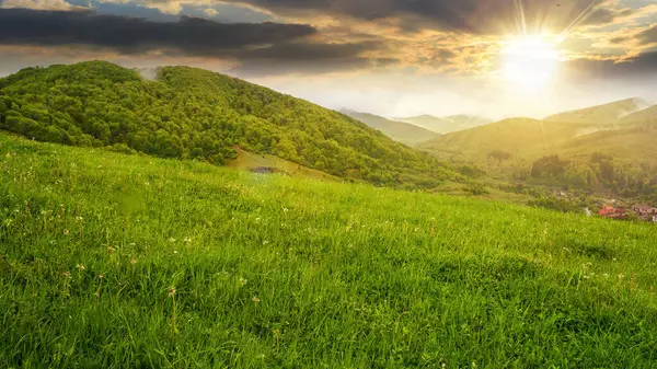 Akşam ışığında dağlık güzel bir kır manzarası. Gün batımında tepede bir orman. Vadinin aşağısındaki köy