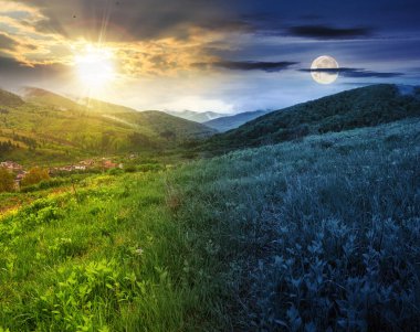 Yaz gündönümünde dağlık kırsal alan. Çimenli çayır manzaralı dağlık arazi ve güneşli ve aylı bir gökyüzünün altında yuvarlanan orman tepeleri. manzara gündüz ve gece zaman kavramını değiştirir.