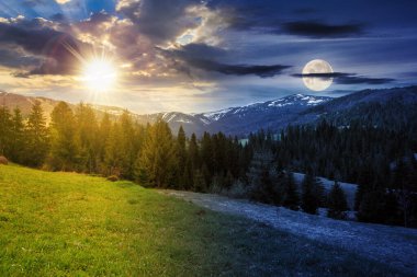 Dağlık bölgede tepede çimenli çayır ve ladin ormanlarıyla kaplı gökyüzünde güneş ve ay olan bir manzara. Bahar ekinoksunda gece ve gündüz konsepti değişir. Sabah ışığında gizemli bir manzara.