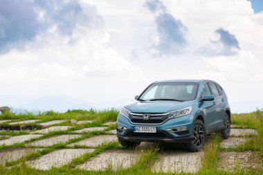 Lypovets, Ukrayna - 22 Haziran 2019: dağın tepesindeki beton yol kenarındaki arazi aracı. kırsal seyahat konsepti. Yazın güzel doğa manzarası Dramatik gökyüzü