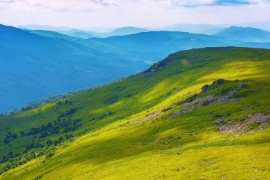 Yaz dağı manzarası. Çimenli yamaçtaki taşlar. Güneşli bir günde, benekli ışıkta güzel bir manzara. Açık hava maceraları konsepti. Alp dağları