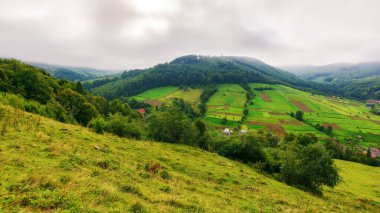 Sonbaharda dağlık kırsal alan. Tepedeki çimenli çayır. Uzak vadideki köy. Kırsal alan. Bulutlu gökyüzü ile yağmurlu hava