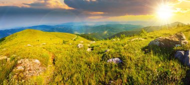 Gün batımında dağ sırasının tepesindeki beyaz taşlar arasında çimenli çayırlarda dar patikalı panoramik manzara. Güzel kırsal manzara Akşam ışığında