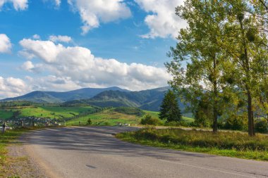 Karpat Dağları 'ndaki eski köy yolu. Sonbaharın başlarında manzara. Akşam ışığında yol kenarındaki ağaçlar. Mavi gökyüzü, uzak Borzhava sırtı üzerinde kabarık bulutlarla