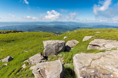Dağ yaz manzarası. Yamacın yamacına yakın bir tepenin tepesindeki çimlerin arasında büyük taşlar olan çayır. Uzaktaki vadiye bak. güneşli hava