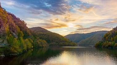 Güneşli bir akşamda dağlarda göl. Orman suya yansıyor. Sonbahar mevsiminde Romanya 'nın güzel manzarası. resim gibi bulutlu bir manzara
