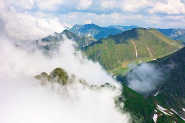 Dağlardaki bulutlar. Güneşli bir yaz gününde Transilvanya Alpleri 'nin yüksek rakımlı manzarası. Çimenli ve karlı dik kayalık yamaçlı bir manzara. Güzel doğa geçmişi. nefes kesici manzara