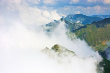 Dağlardaki bulutlar. Engebeli arazi. Güneşli bir yaz gününde Transilvanya Alpleri manzarası. Çimenli ve karlı dik kayalık yamaçlı bir manzara. Güzel doğa geçmişi. Karpatya Devasa