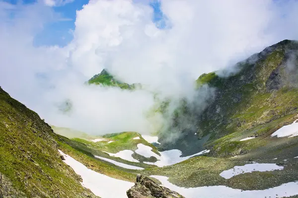 Dağlardaki bulutlar. Güneşli bir yaz gününde Transilvanya Alpleri manzarası. Çimenli ve karlı dik kayalık yamaçlı bir manzara. güzel doğa arkaplanı