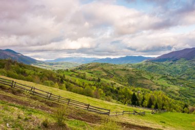 Baharda dağ manzarası. Yamaçtaki çayır. Yuvarlanan tepeleri olan kırsal bir manzara. Gökyüzü akşam ışığında bulutlu. hava değişimi