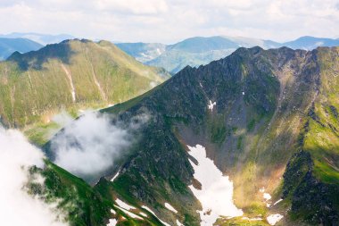 Dağlardaki bulutlar. Uzaktan kumandalı. Güneşli bir yaz gününde Transilvanya Alpleri manzarası. Çimenli ve karlı dik kayalık yamaçlı bir manzara. Güzel doğa geçmişi. görkemli yükseklik