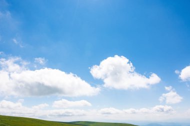 Mavi gökyüzünde beyaz kümülüs bulutları. Dağların tepesinde ufukta. Atmosfer durumunun gün ışığında harika bir arka planı var. Parlak yaz hava tahmini. Temiz hava.