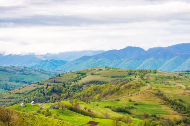 Baharda dağlık kırsal alan. iklim Karpati. Tepelerdeki ağaçlar ve tarımsal tarlalar uzak vadiye doğru akıyor. Bulutlu bir gökyüzünün altında, benekli ışığın altında. Açık hava macerası