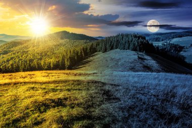 Alacakaranlıkta güneş ve ay ile birlikte kozalaklı ormanın yakınındaki çimenli çayır ile dağlık bir arazi. Gündüz ve gece zaman kavramını değiştirir. Gizemli kırsal manzara Sabah ışığında