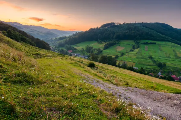 Yazın kırsal alan. Yeni bir sabah. Şafakta vadideki köy. Kızıl gökyüzünün altındaki tepede orman ve yeşil çayır. Ukrayna dağlarının manzaralı manzarası.