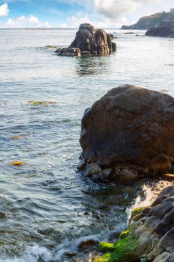 Suda kaya olan deniz manzarası. Sabah ışığında sakin deniz yüzeyini yansıtan desenli kaya. Yazın tatil sezonu. Güneşli bir hava. Ufukta kabarık bulutlar