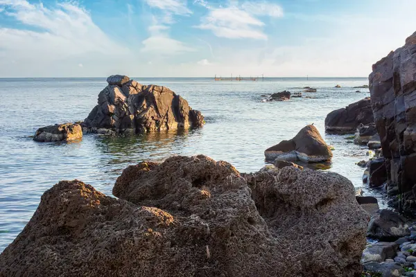 Suda kaya olan deniz manzarası. Sabah ışığında sakin deniz yüzeyini yansıtan desenli kaya. Yazın tatil sezonu. Güneşli bir hava. Ufukta kabarık bulutlar