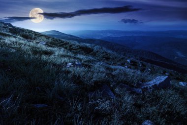 Yazın geceleri dağlık arazinin manzarası. Tepede çimenler ve bulutlu mavi gökyüzü olan açık hava arka planı. Dolunay ışığında muhteşem Karpat Alpleri 'nde yürüyüş yapmak