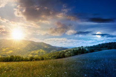 Yaz gündönümünde güneş ve ay ile geniş çayırlı dağ manzarası. Çayırdaki çimenler kırsal alandaki tepelerden uzak Alp Vadisi 'ne yuvarlanıyor. Gündüz ve gece zaman kavramını değiştirir