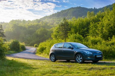 Pepechyn, Ukrayna - 10 Haziran 2020: kırsal yolda araba. Sabahın ilk ışıklarıyla manzara. Yaz mevsiminde Transcarpathia 'ya seyahat. Tepedeki yeşil yaprak döken orman.