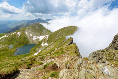 Yazın uzak gölü olan dağ manzarası. Güneşli bir günde Romanya 'nın doğasını gezmek. İbneler tepesinin üstündeki mavi gökyüzündeki bulutların manzarası. Avrupa 'da tatil sezonu. Huzurlu vahşi doğa
