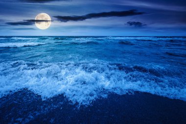 Gece fırtınadan önce deniz gelgiti. Dolunay ışığında ıslak kumlu sahilde köpüklü dalga sıçraması. Kadife mevsiminde rüzgarlı bir hava. dramatik deniz manzarası arkaplanı